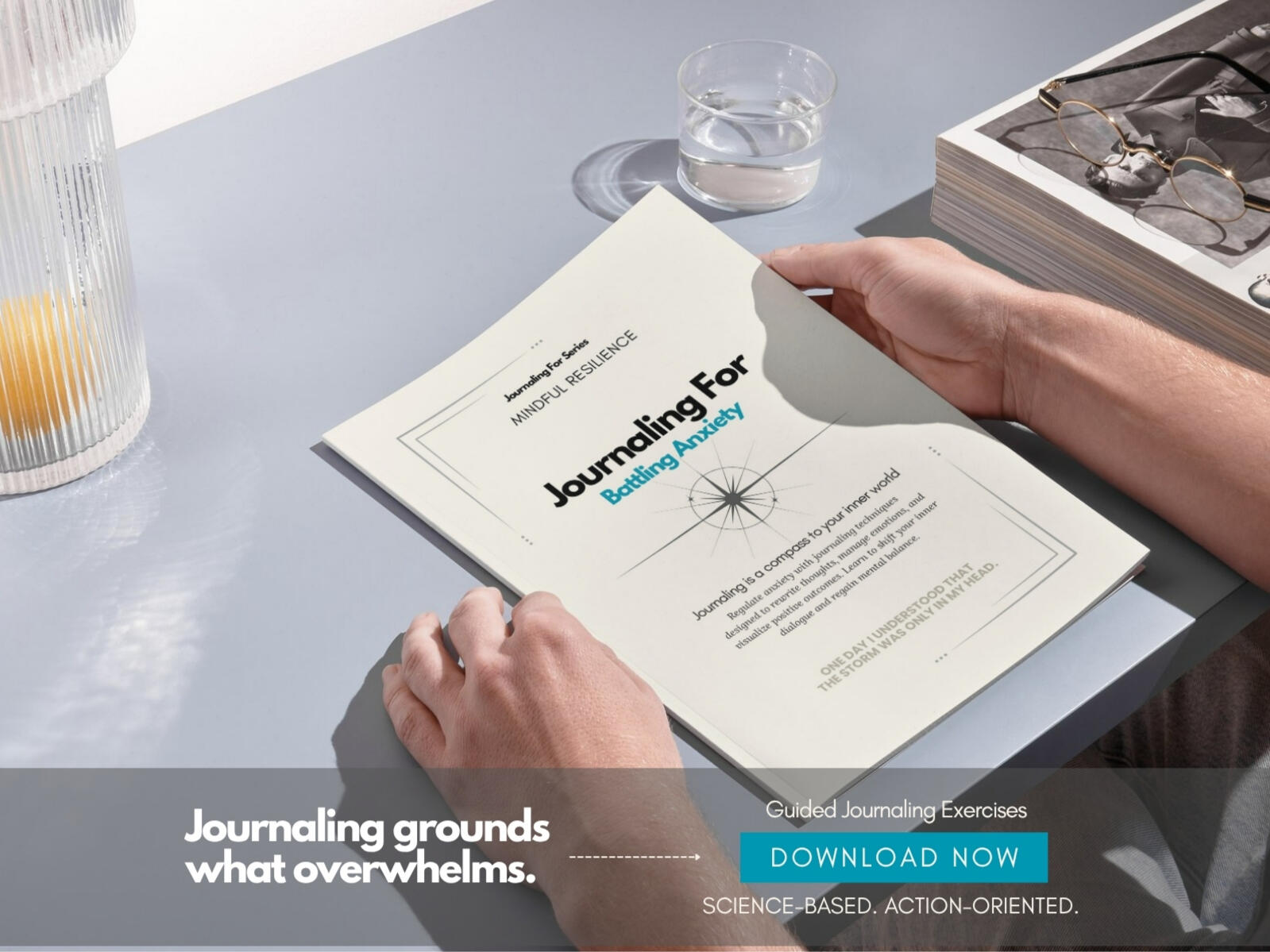 Person holding the ‘Journaling For – Battling Anxiety’ workbook on a sunlit table next to a glass of water and a journal stack.