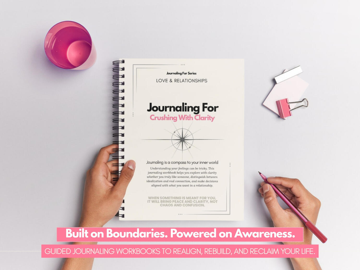 Journaling For – Crushing With Clarity’ spiral-bound workbook held by a person on a soft-toned desk with pink stationery accents.